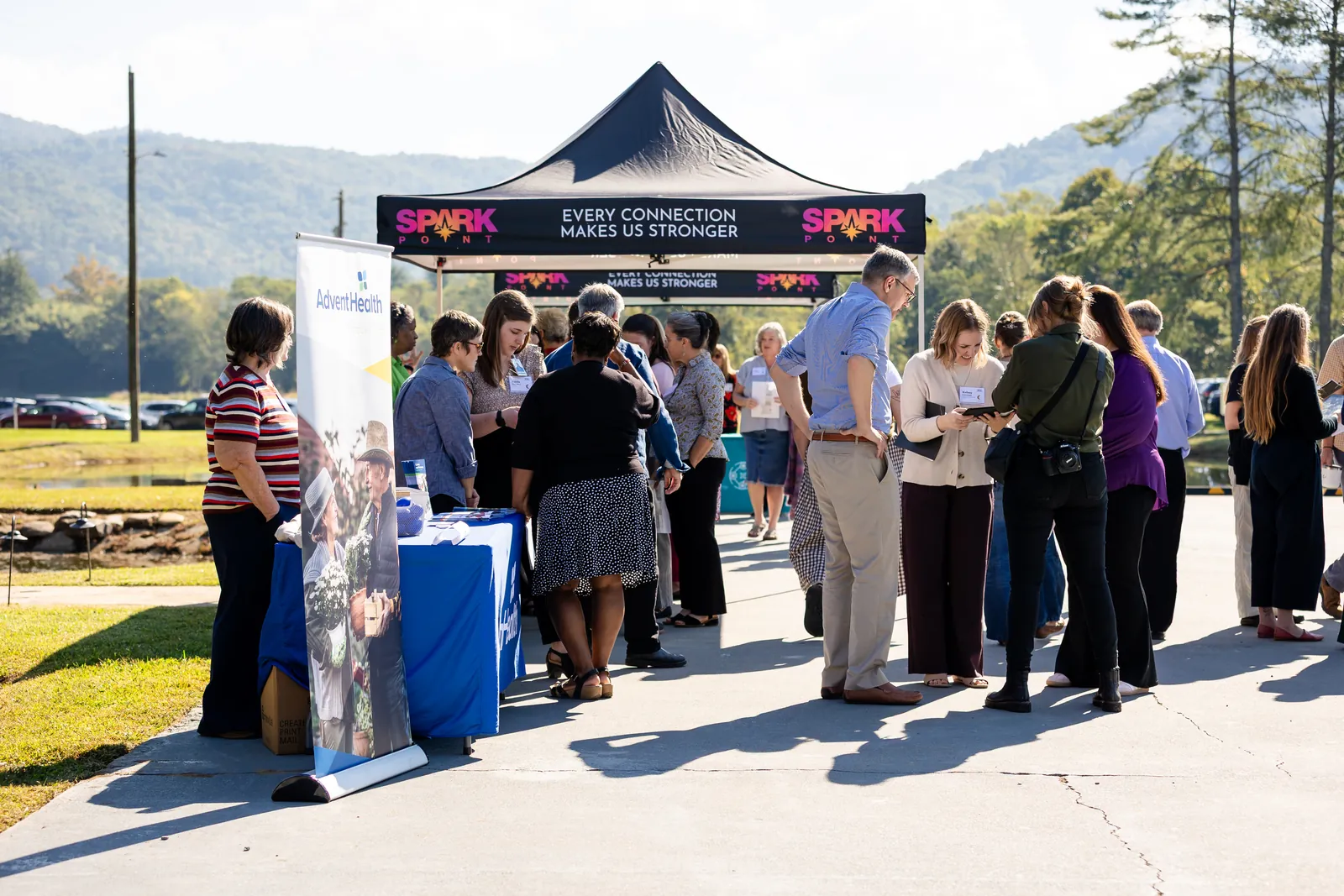 Attendees gather under a SparkPoint tent whose banner reads “Every connection makes us stronger,” with the mountains behind them.