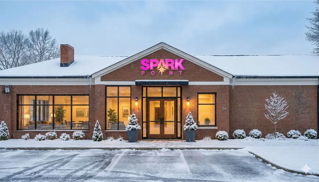 Concept rendering of the Transylvania Resilience Hub in winter: a brick building with a glowing SparkPoint sign, lit windows, and snow on the ground.