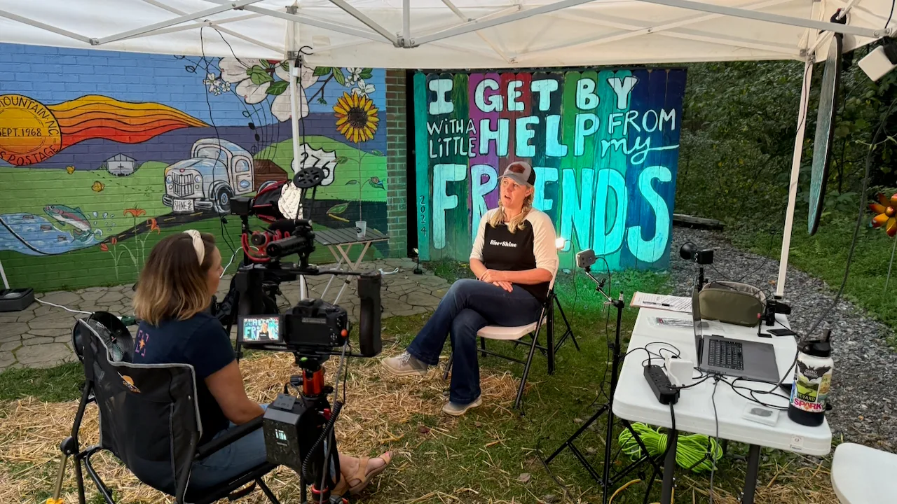 A SparkPoint crew filming a community interview on location, in front of a mural reading 'I get by with a little help from my friends.'